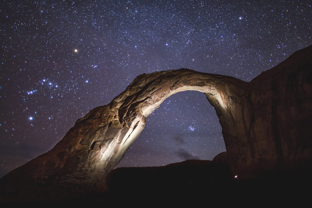 Rock Arch lit with lights under a star filled night sky.