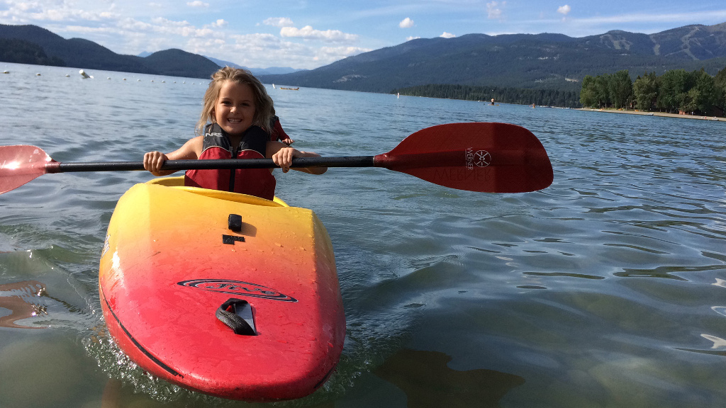 Child on the water in a kayak with mountains in the background.