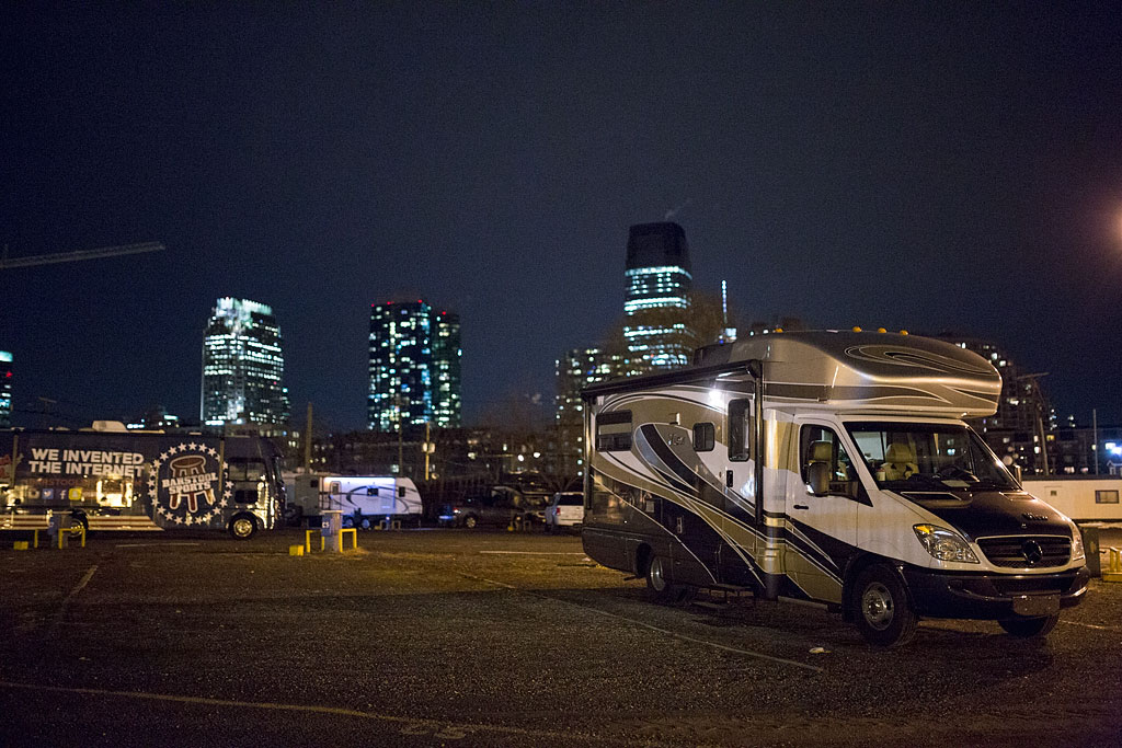 Winnebago View parked in a parking lot with a night sky above and a bright city skyline behind.