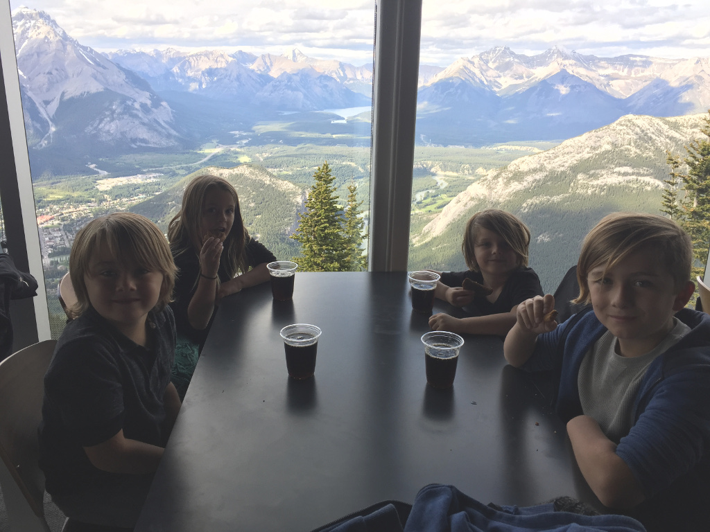 Four kids at a table with a breath-taking view of the mountains below out the window.