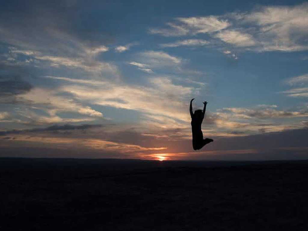 Silhouette of woman jumping in air as sun sets in the background.