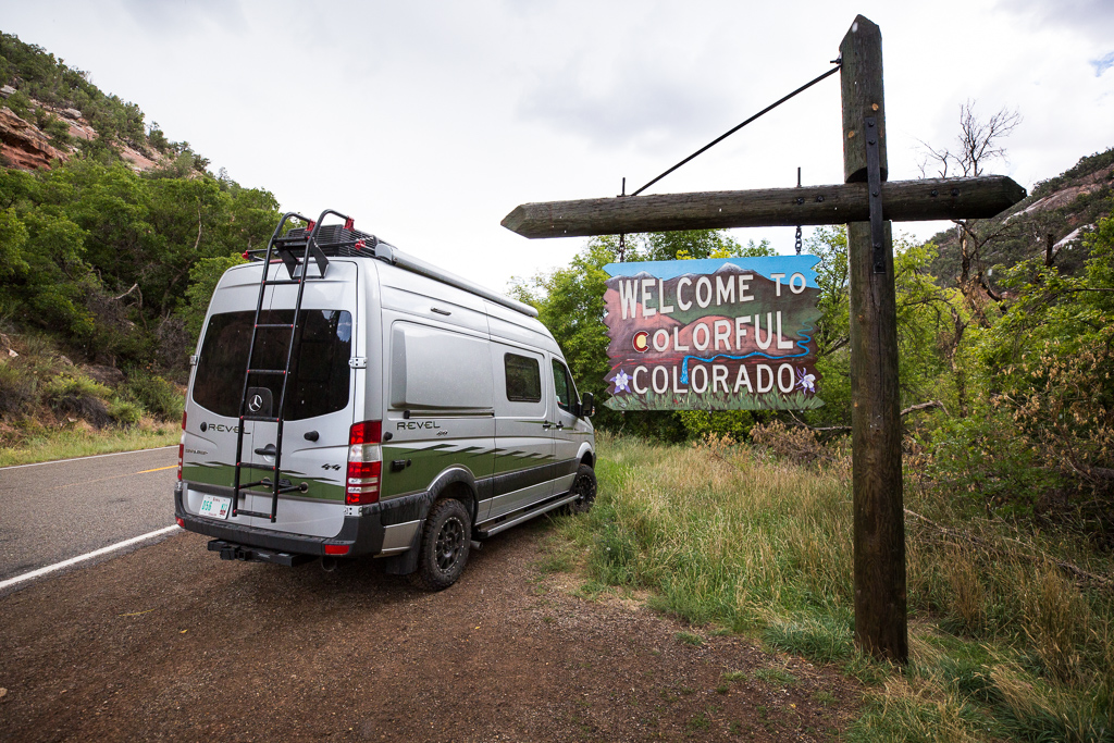 Winnebago Revel parked at the side of the road next to sign that reads, "Welcome to Colorful Colorado."