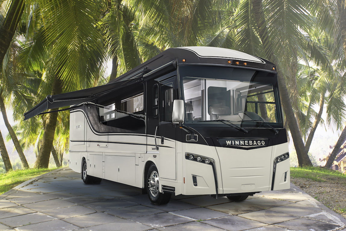 Winnebago Horizon with awning out on parking pad beneath palm trees.
