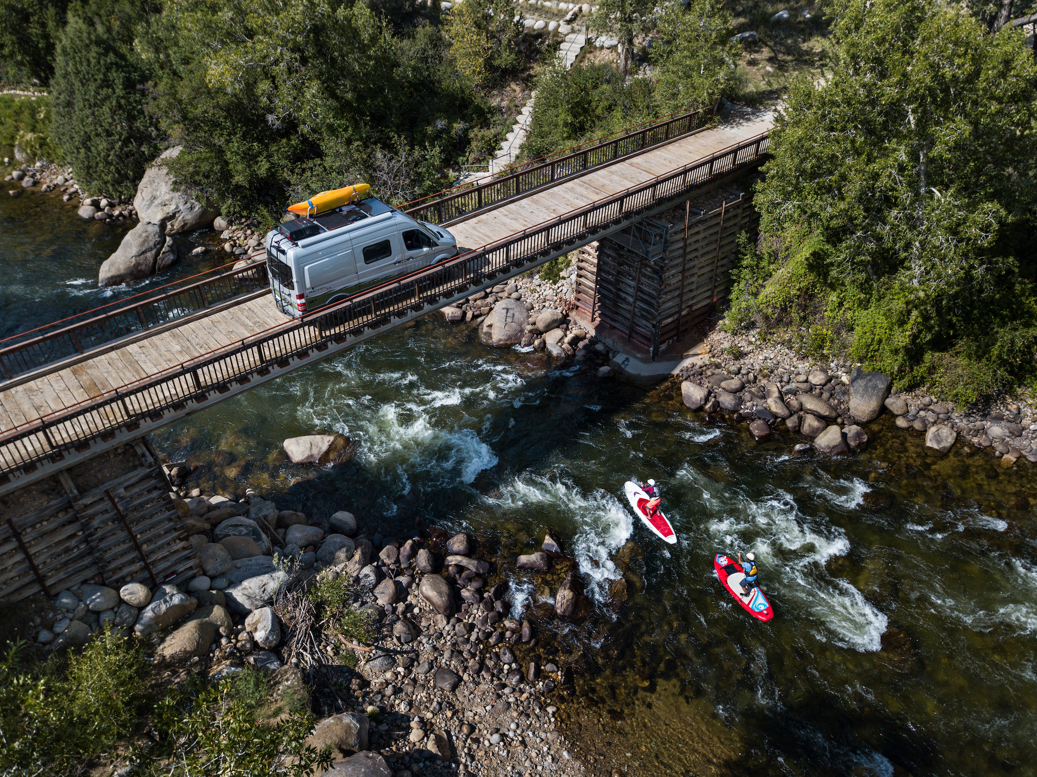 Winnebago Revel parked on a bridge with paddle boarders passing on the water running below.