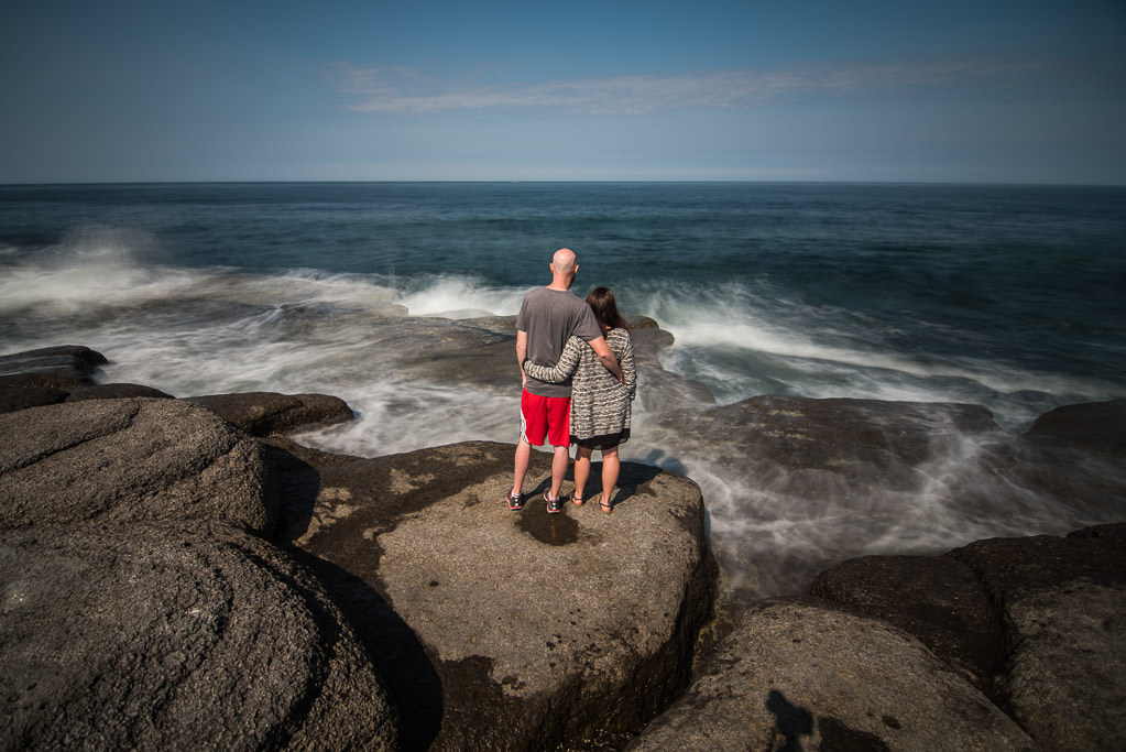 Couple standing on rocks along the water
