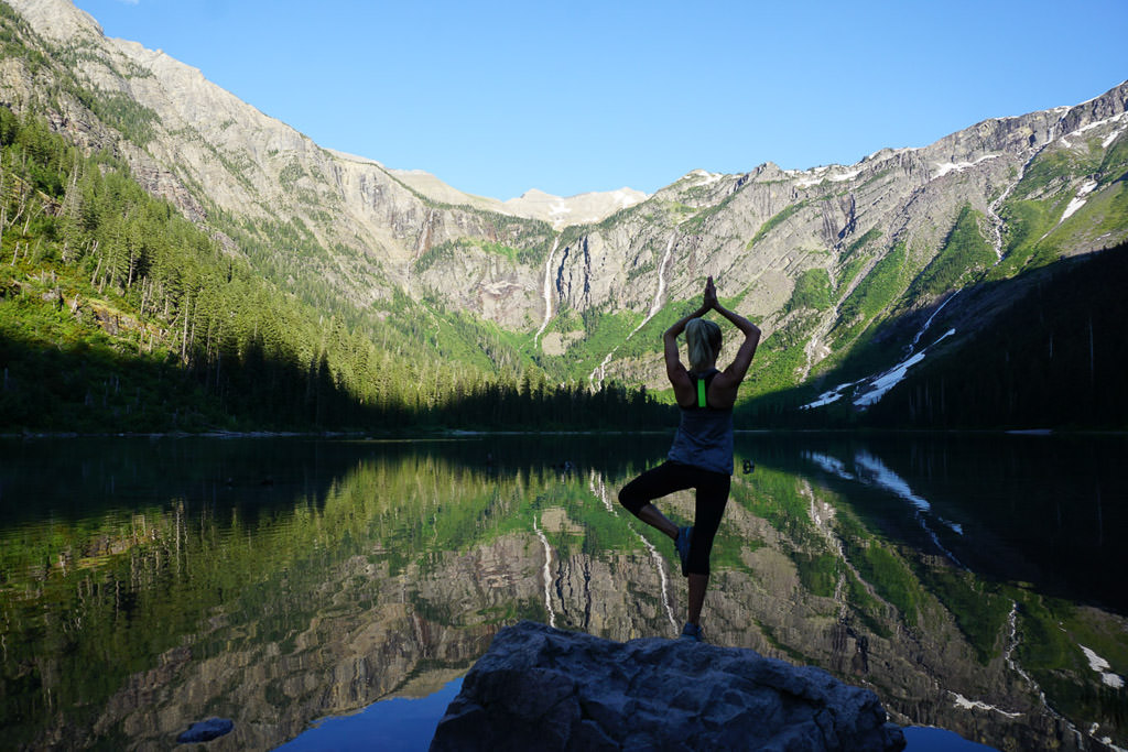 Woman doing yoga pose on top of a rock overlooking lake and mountains.
