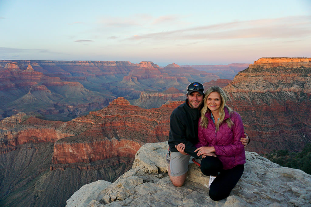 Lindsay and Dan kneeling at the edge of a cliff with canyons stretching as far as the eye can see behind them.