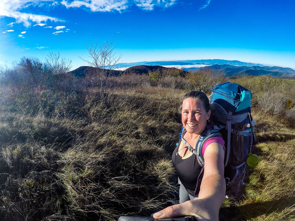 Selfie of Kathy with blue skies above and mountain range behind her.