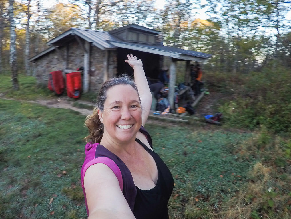 Kathy smiling with a shelter behind her.