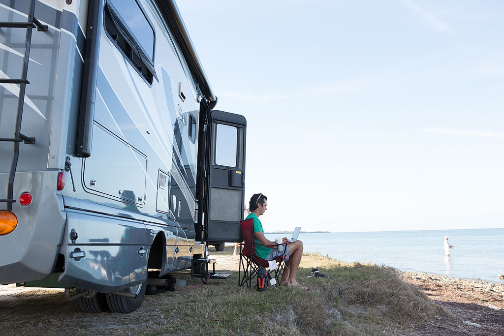 Jordan working on laptop outside their Winnebago View while parked along the ocean.