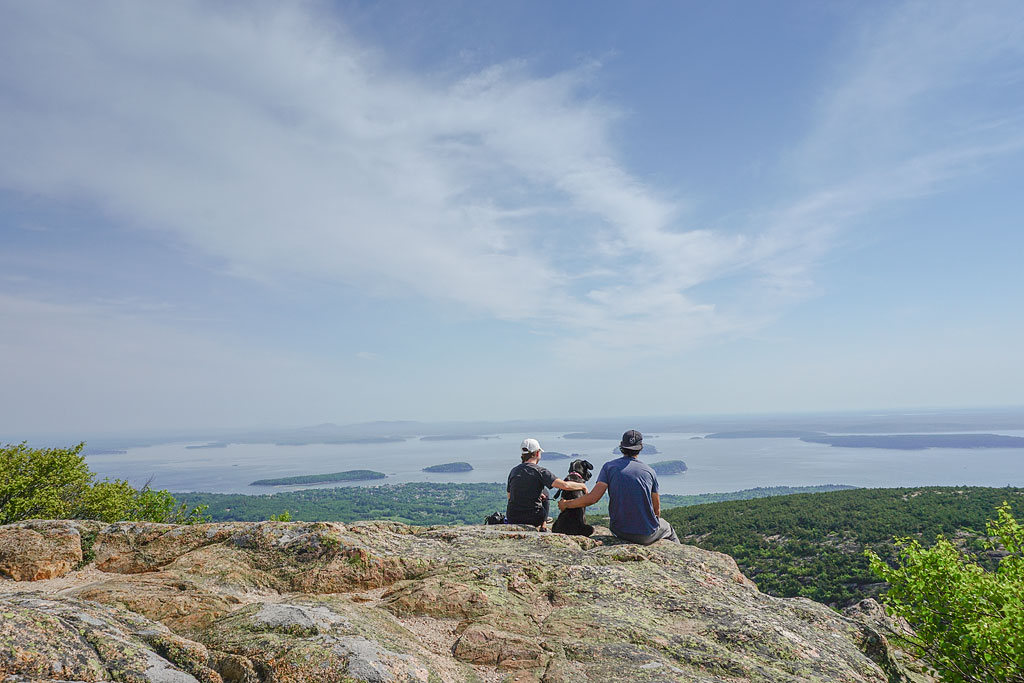 Jordan, Brittany, and Ella sitting on a rock overlooking the water at Cadillac Mountain.
