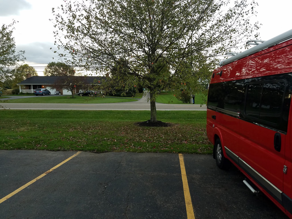 Winnebago Travato parked in parking lot with residential home across the street