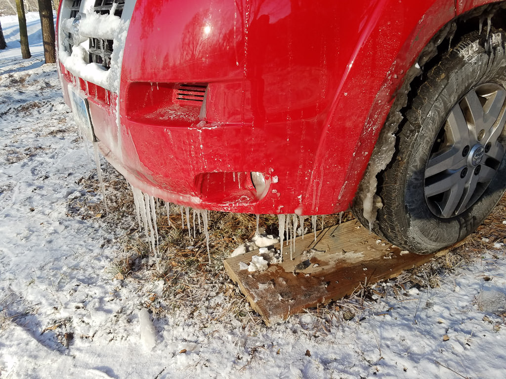 Front end of red Winnebago Travato covered in ice