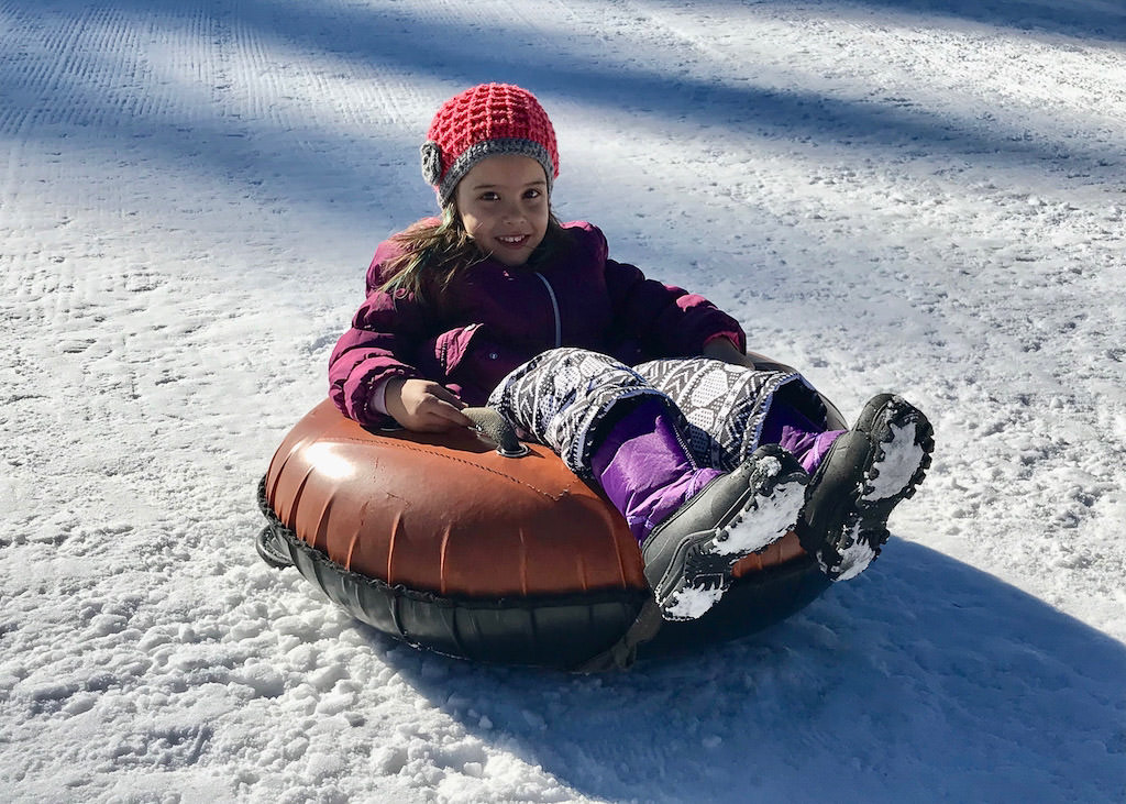 Child on snow tube at the bottom of a snowhill.
