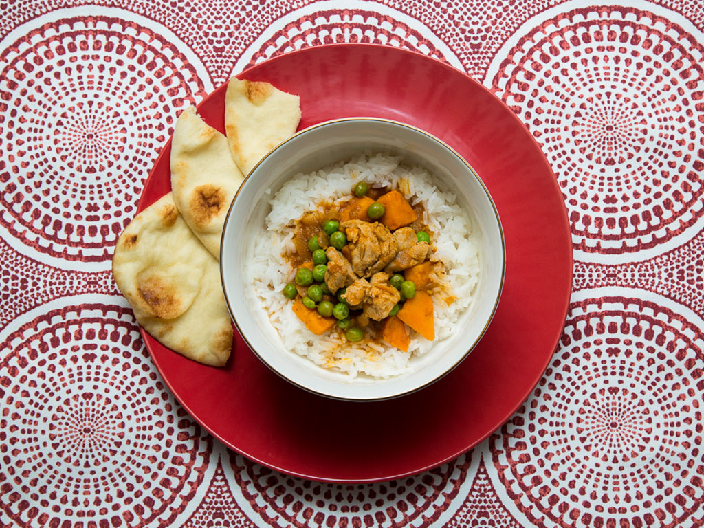 Chicken curry in a bowl with pieces of pita on a red plate
