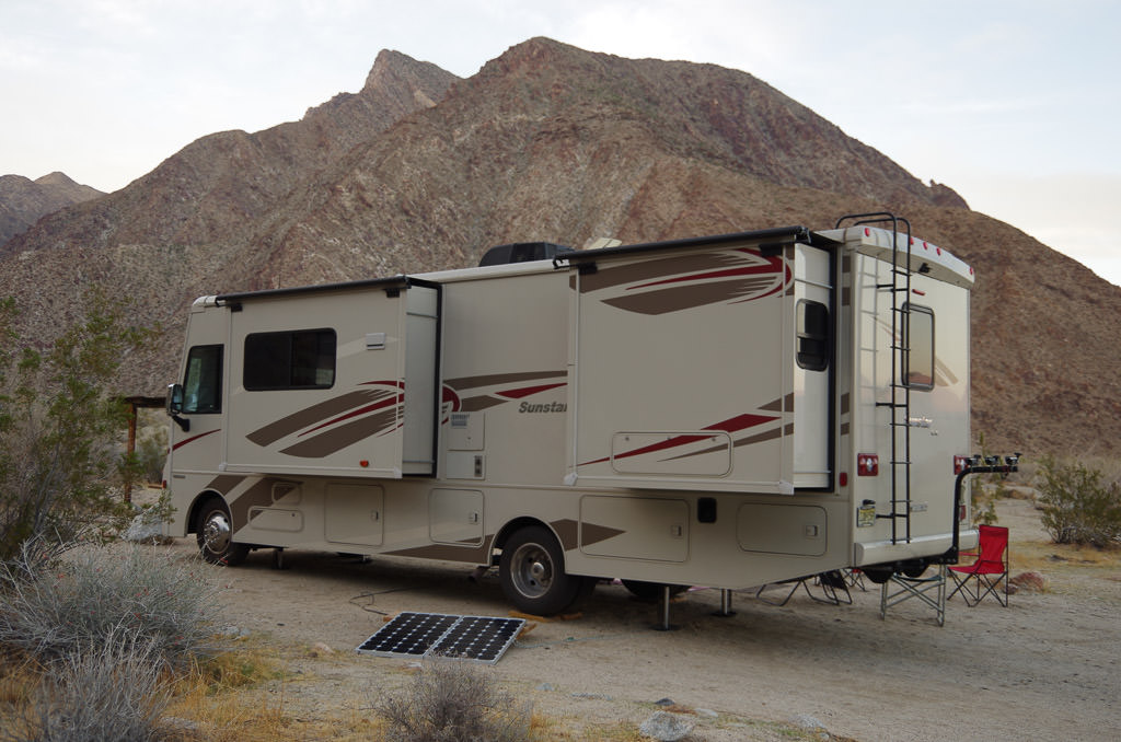 Winnebago Sunstar driver's side view of exterior, parked in camp w/portable solar on dispaly