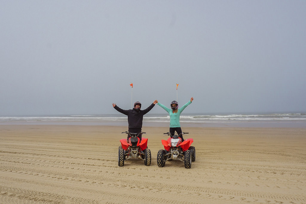 Couple on ATVs on the sand with ocean in the background