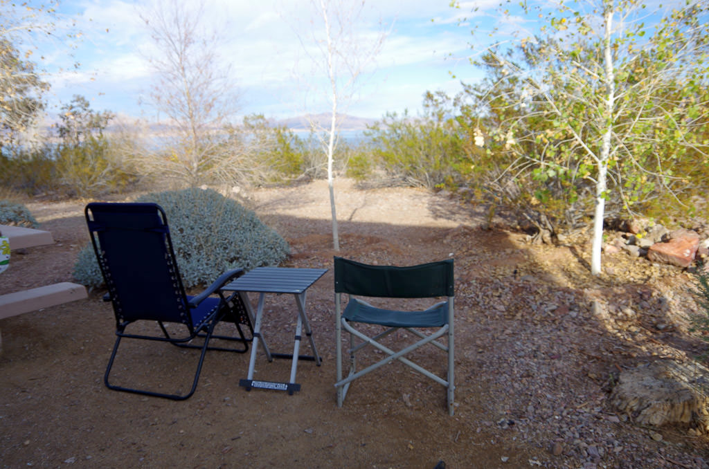 Two camping chairs looking out to a wooded area with water in the background