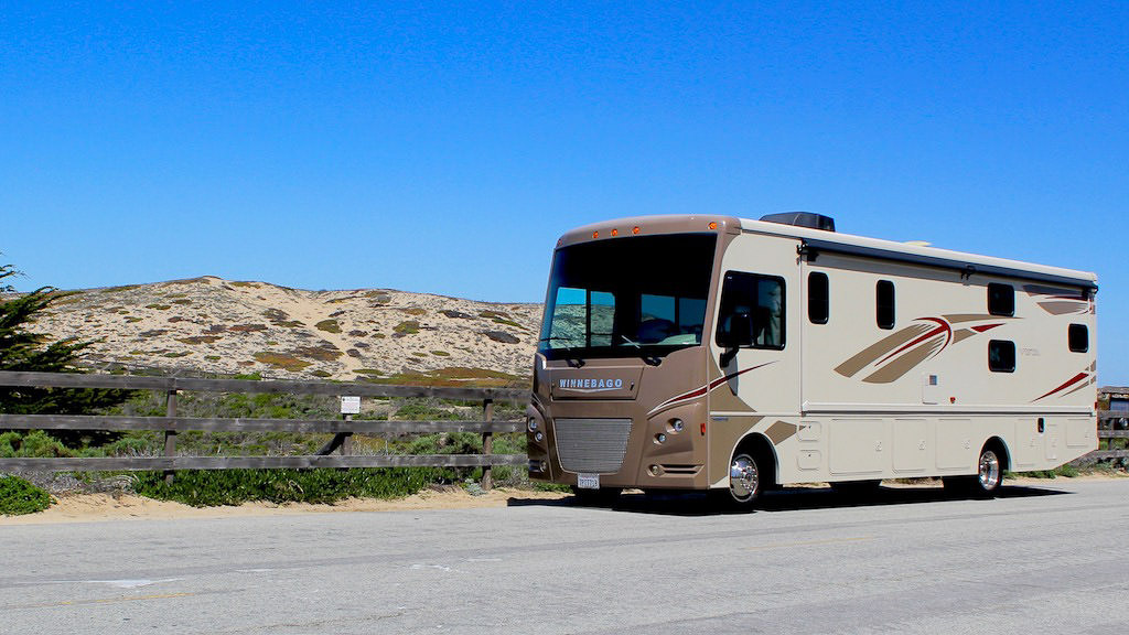 Winnebago RV parked on the side of the road with a sandy hill behind