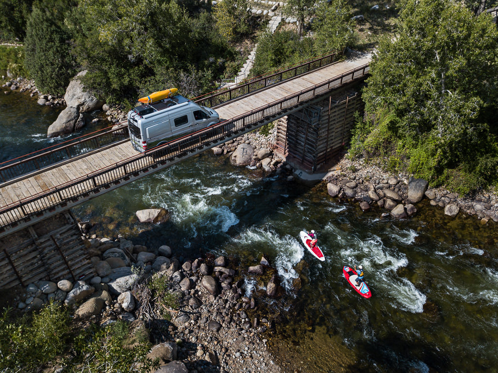 Winnebago Revel parked on a bridge with paddle boarders passing on the water below.
