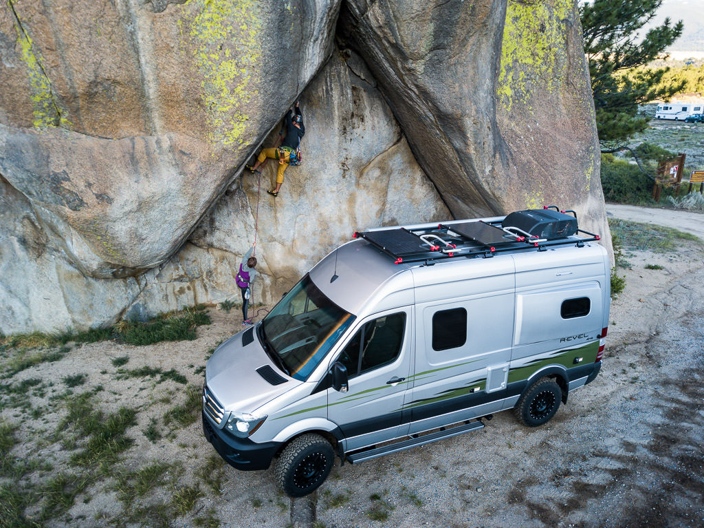 Winnebago Revel parked at base of a rock structure, with two people climbing. 