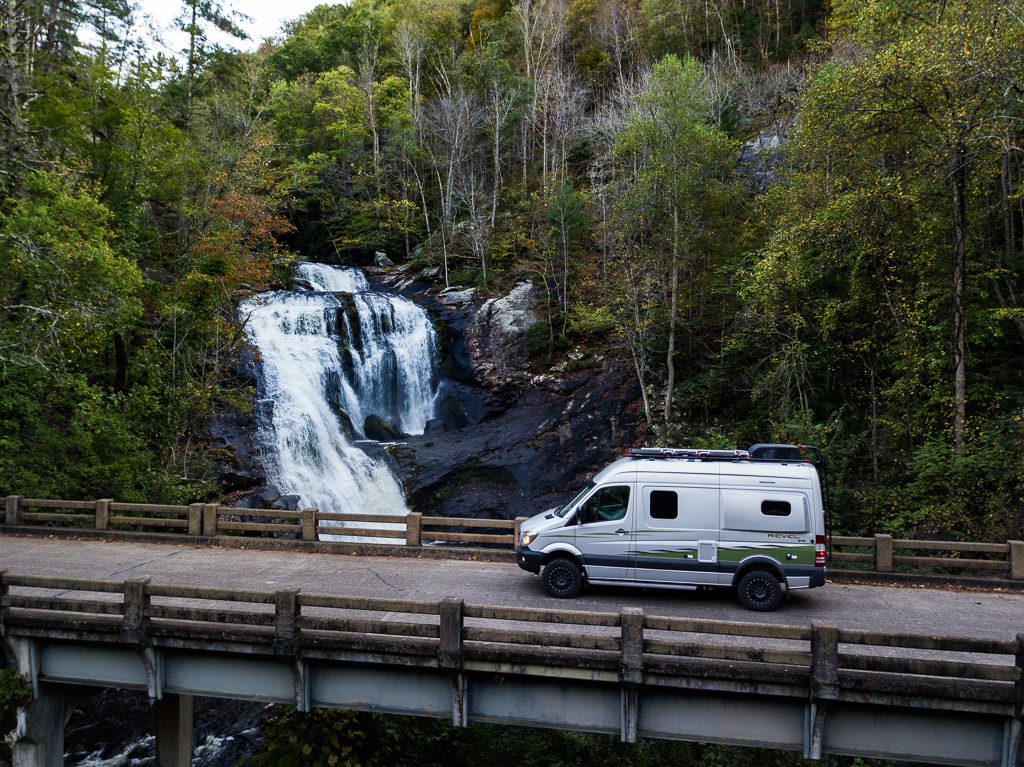 Winnebago Revel parked on a bridge with a waterfall cascading down the hillside.
