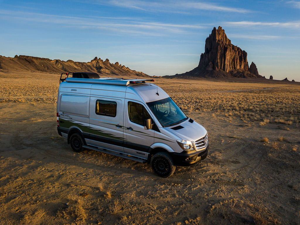 Winnebago Revel parked on the sandy landscape with rock formations behind it.