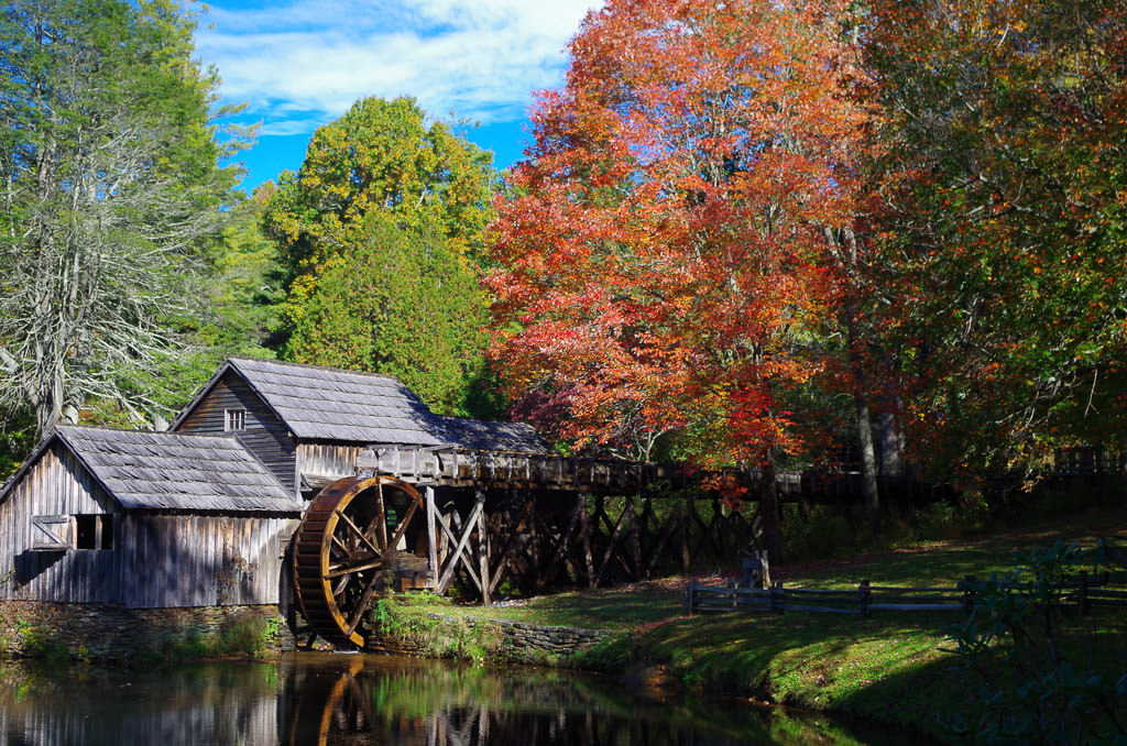Old mill with water below and trees with many colors surrounding