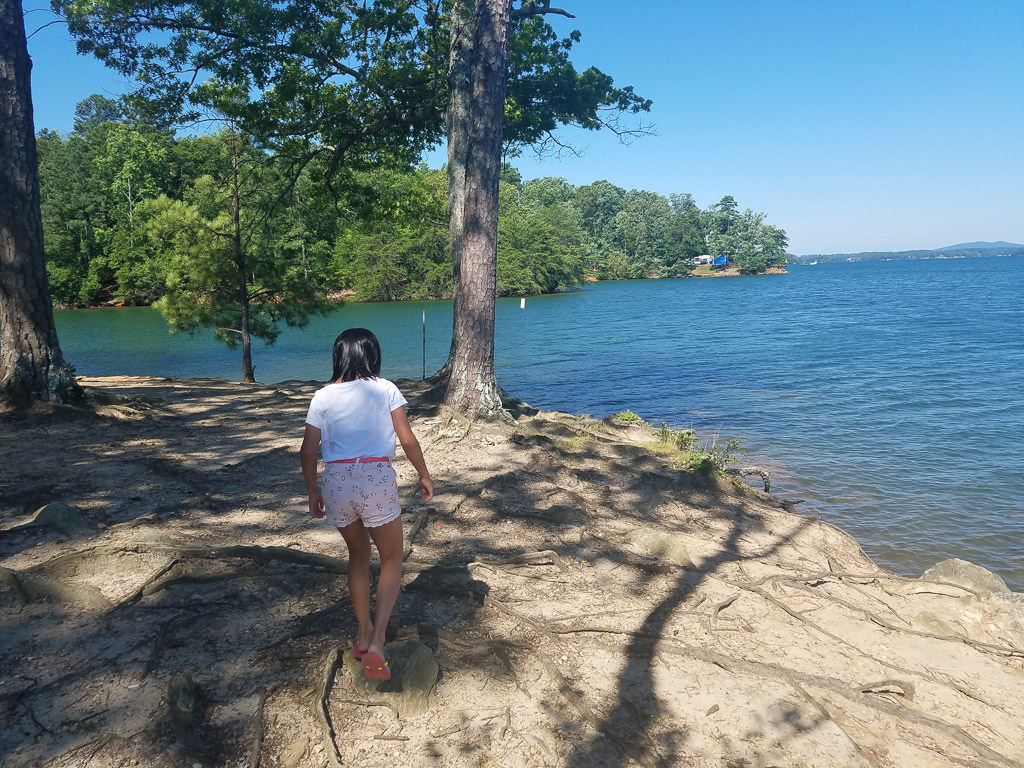 Younger girl walking on shore along water with trees around