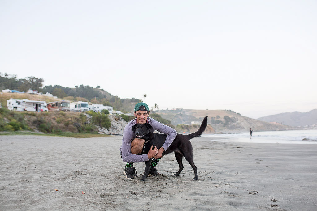 Jordan hugging their dog on a sandy beach