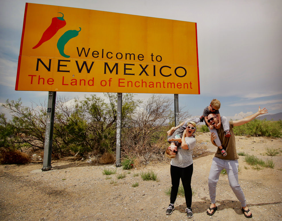 Nic and Jess with Bailey and Brady on their shoulders standing beneath the Welcome to New Mexico sign.