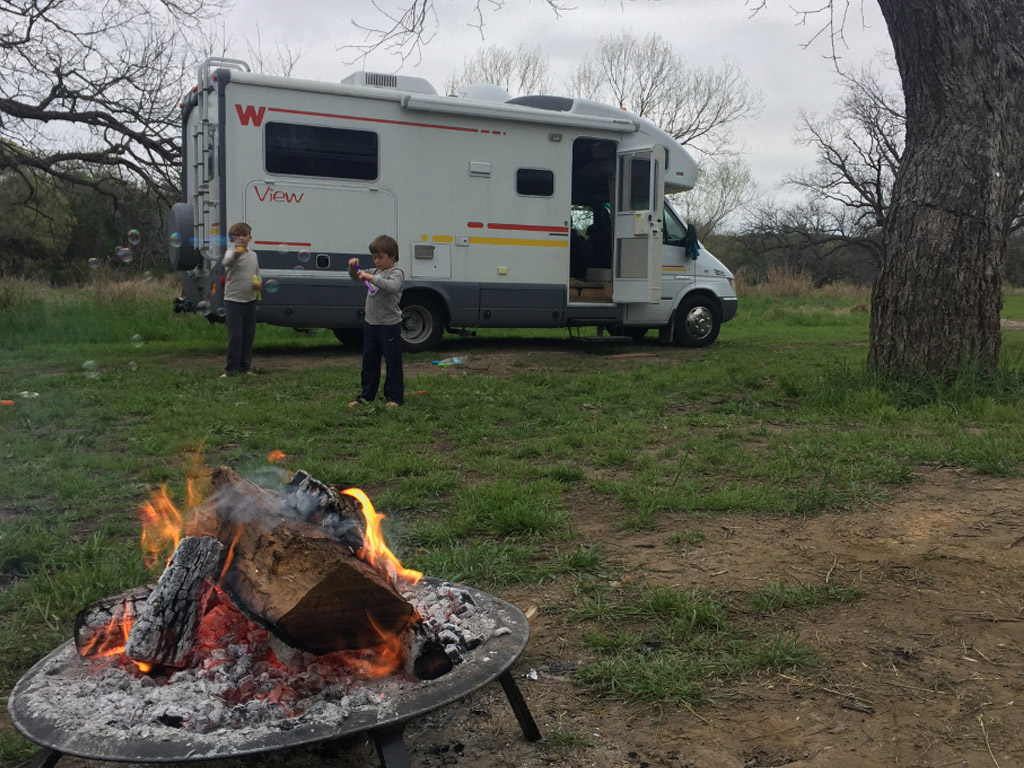 Kids playing outside a Winnebago View with a campfire going.