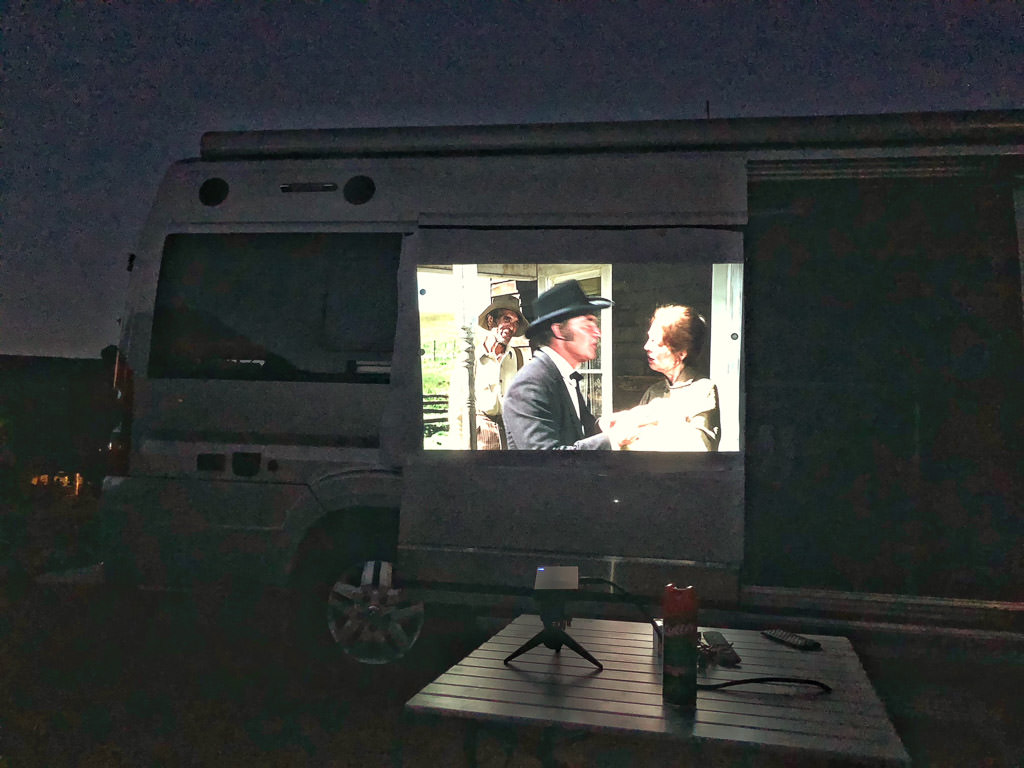 Movie playing on a projector on side of a Winnebago Travato.