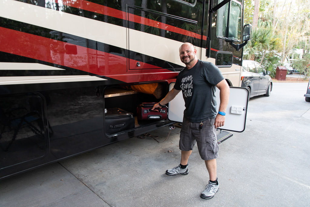 Kenny pulling luggage from outside storage compartment of Winnebago Adventurer.