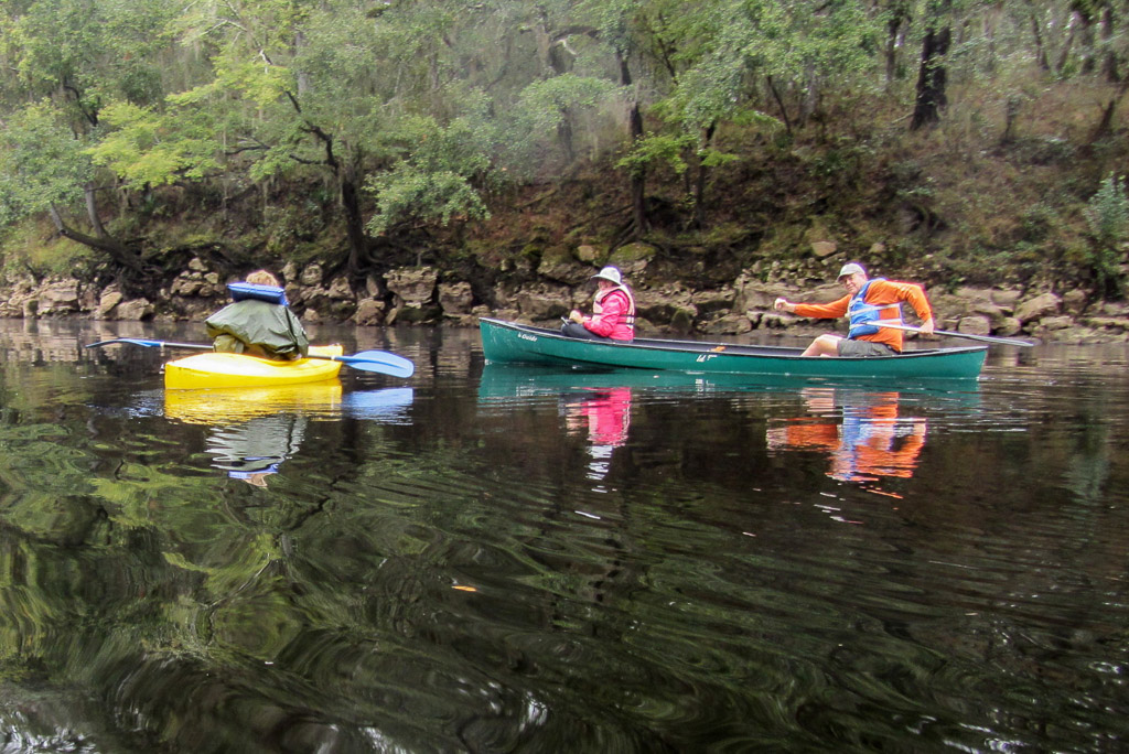 A kayaker and two people in a canoe going down the river.