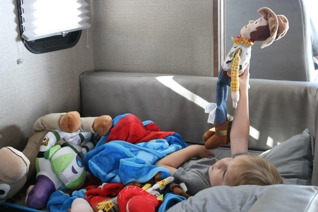 One of the kids laying in bed playing with his stuffed toys