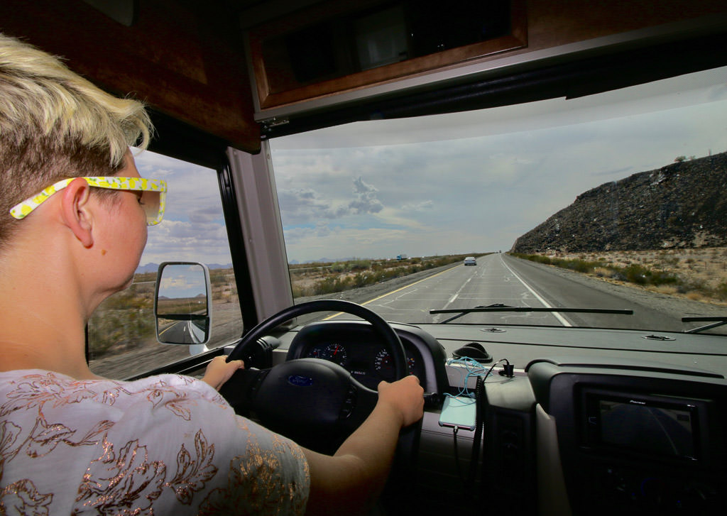 Jess driving down a highway with tall hills to the right and plains to the left