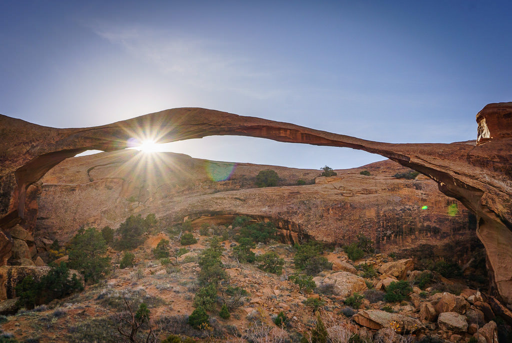 The landscape arch with sun peaking between the rocks and the arch.
