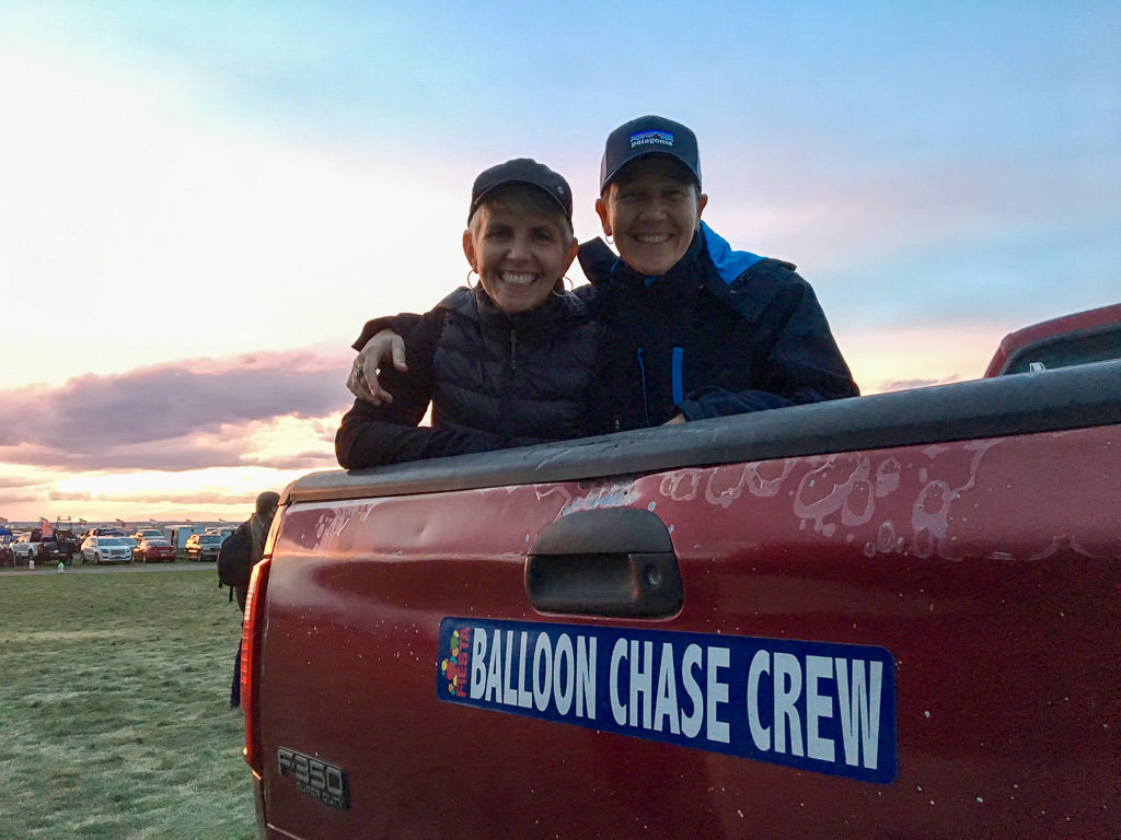 Noel and Chris smiling by sign on back of truck that says "balloon chase crew."