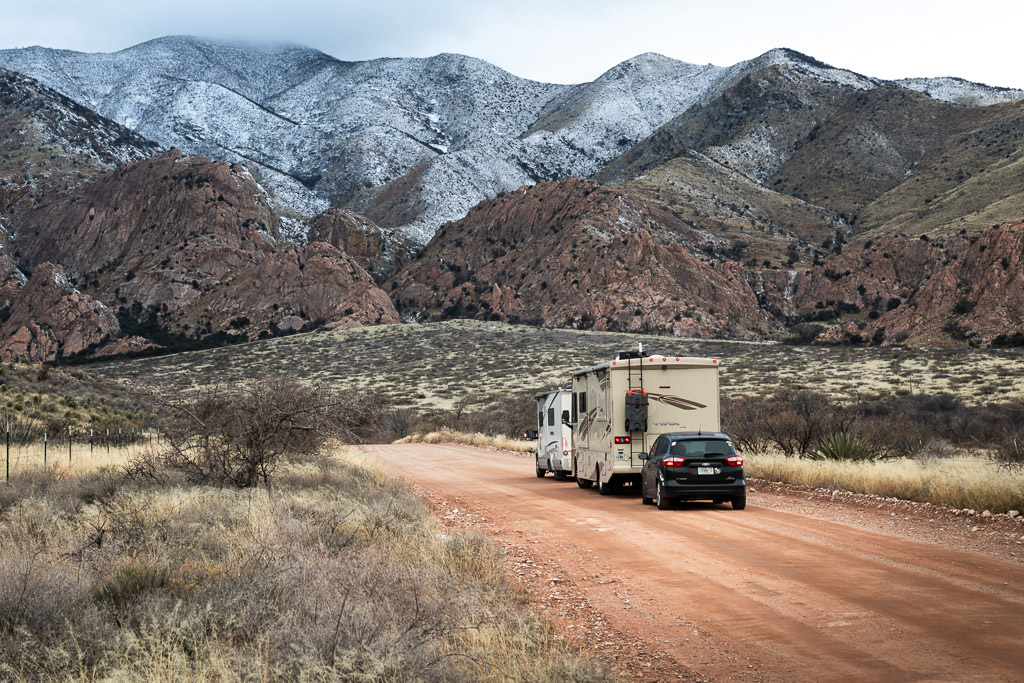 Winnebago Trend being followed by Winnebago Vista towing a car heading towards the mountains on a dirt road.