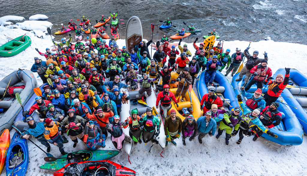 Large group of people on the edge of the river posing with their rafts and kayaks