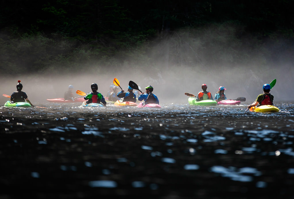 Kayakers in a group floating across a smooth part of the river in the fog.
