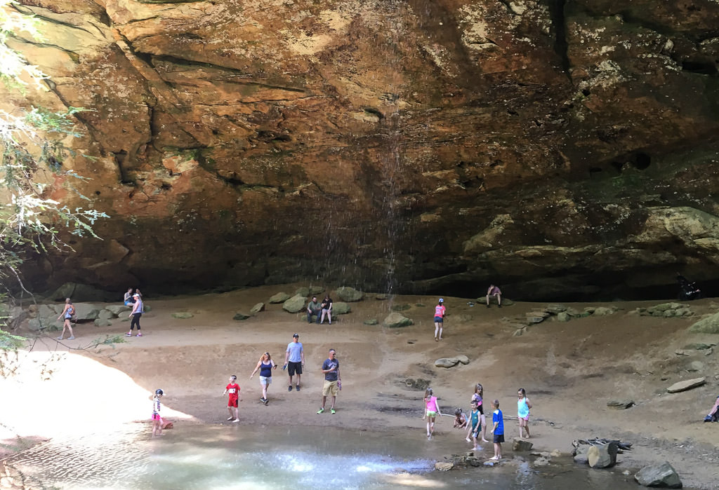 People gathered beneath a rocky overhang playing in the water.