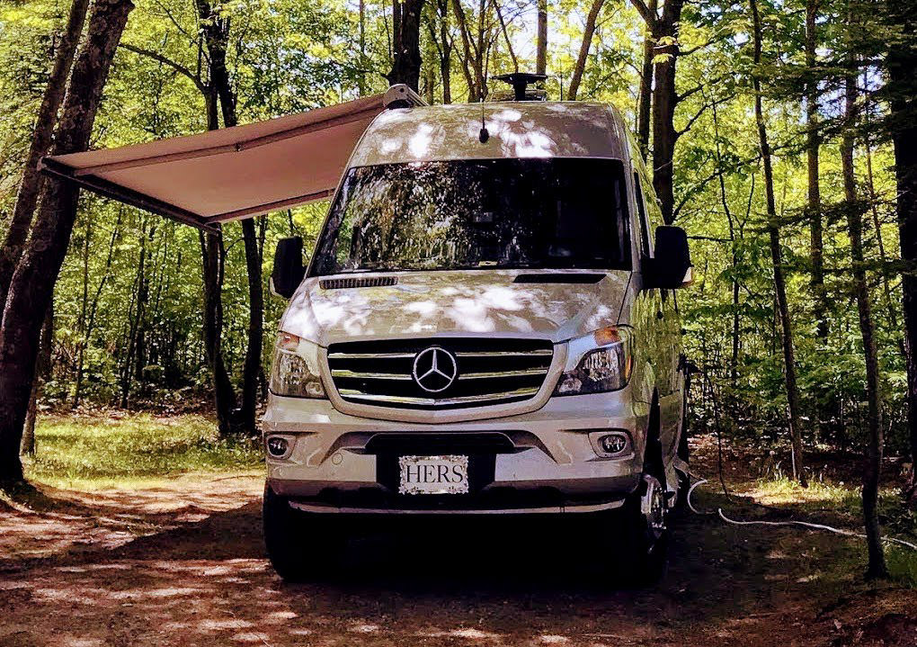 Winnebago Era with awning out parked in tree surrounded campsite.