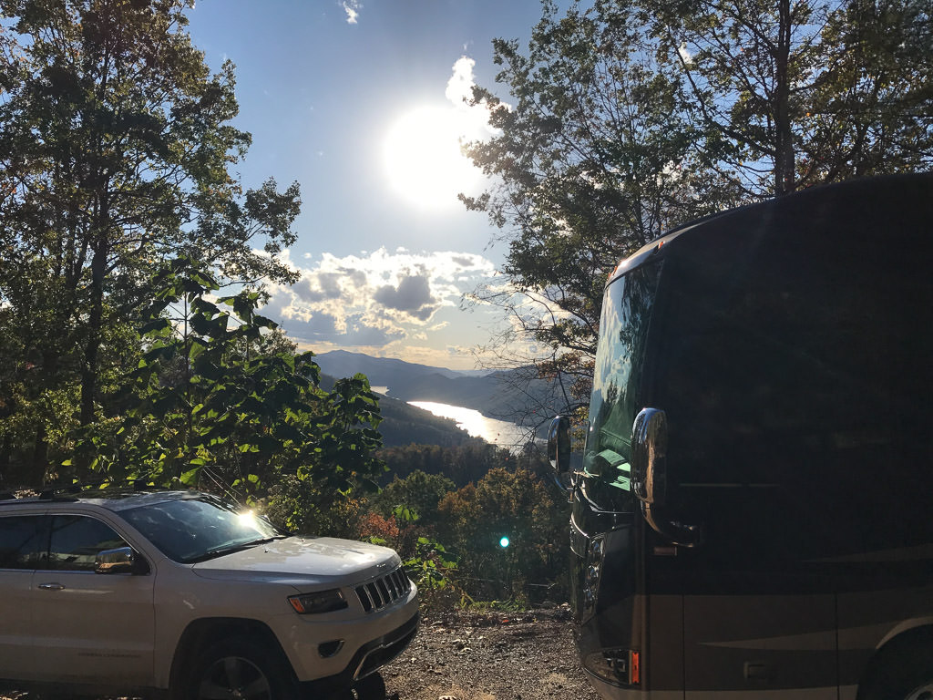 Winnebago Ellipse parked at the edge of a drop off with view of a river and mountains through the trees.