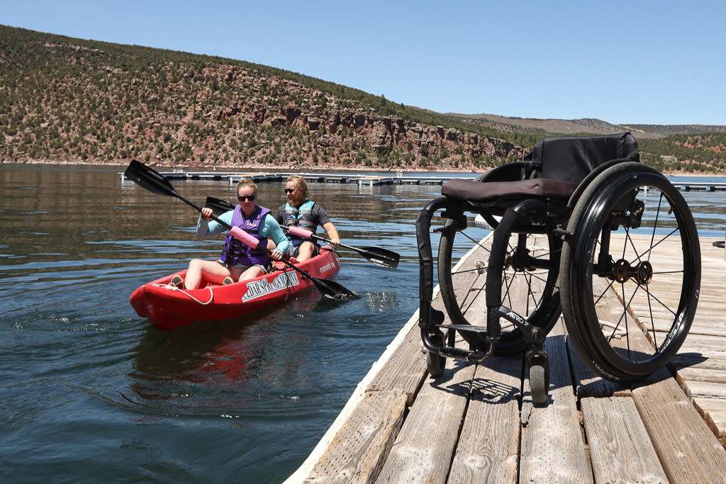 Nerissa and friend in kayak with empty wheelchair on the dock.
