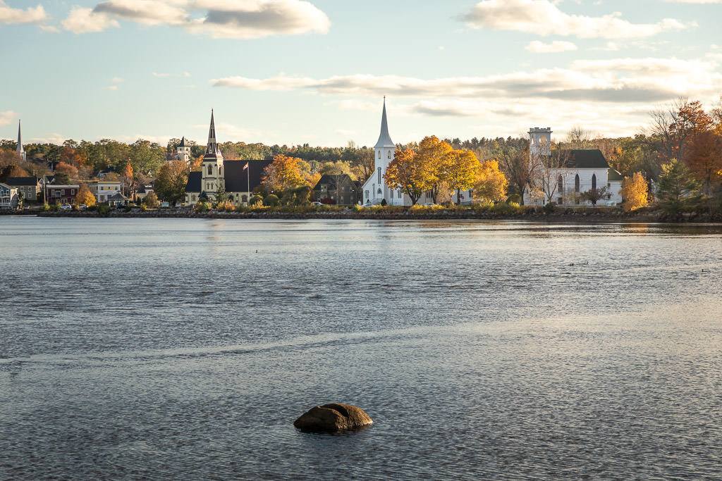Three churches along Mahone Bay with trees of all colors surrounding. 