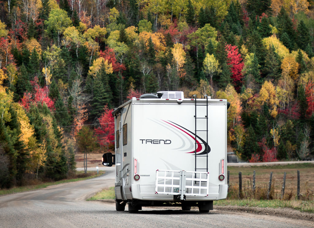 Winnebago Trend driving on a road towards all colors of trees.