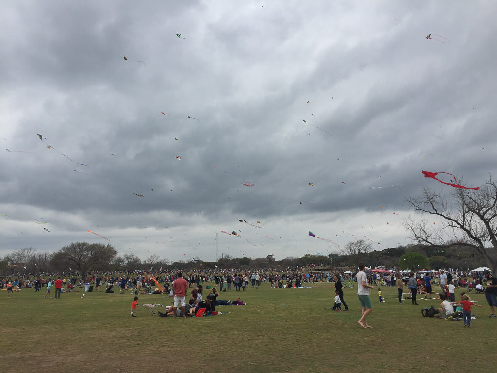 Crowd of people gathered flying kites at the Zilker Kite Festival.