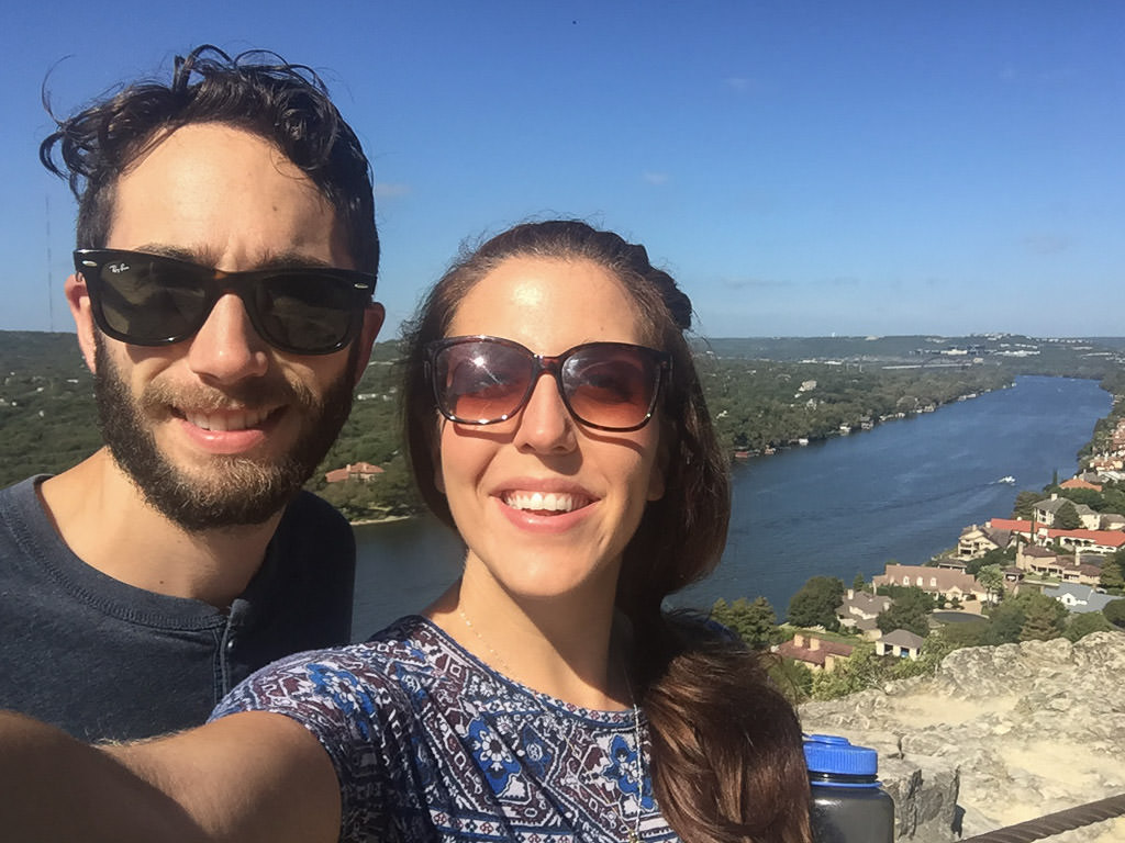 Couple posing at the top of Mount Bonnell with view of the water behind.